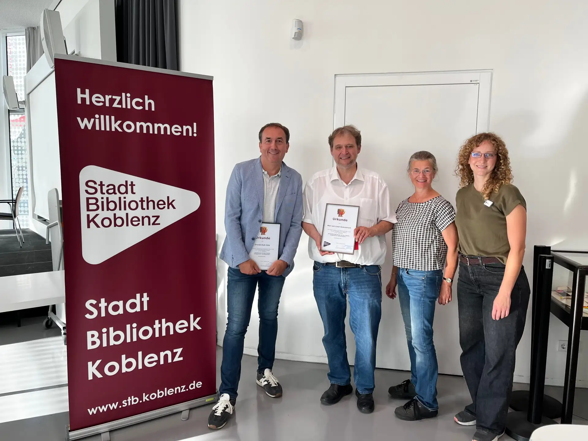 Gruppe von Personen mit Preis bzw. Preisschild vor einem Gebäude, im Rahmen der Auszeichnung der Gewinnerschulen.