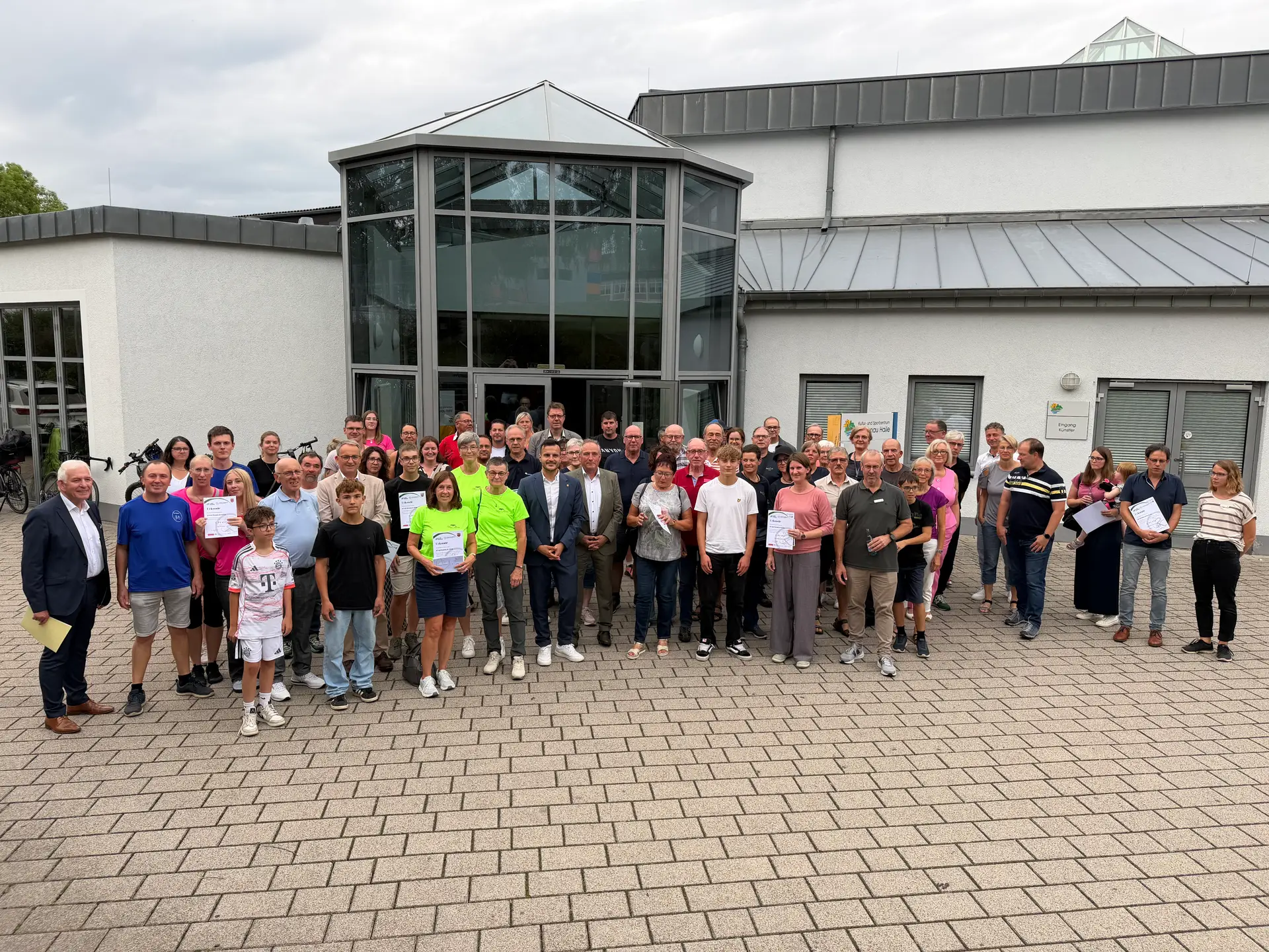 Mehrere Personen stehen in einer Halle bei einer Veranstaltung, im Vordergrund ein Tisch- bzw. Veranstaltungsbereich.