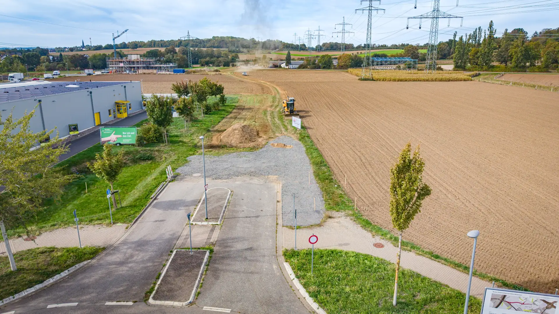 Luftaufnahme einer am Feldrand endenden asphaltierten Straße neben einem Gewerbegebäude.