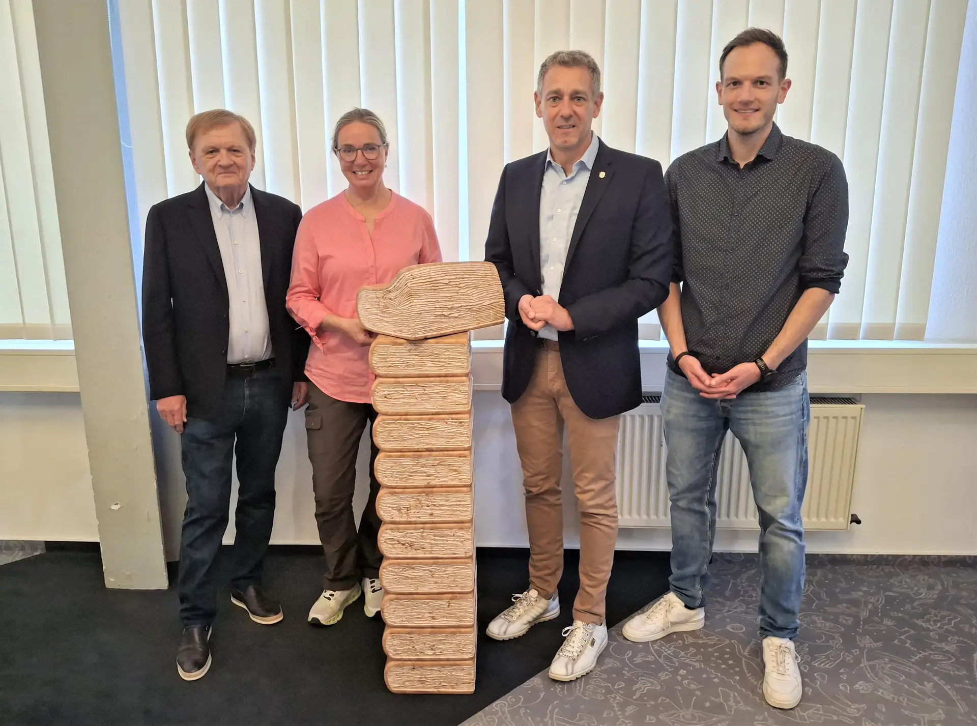 Vier Personen posieren nebeneinander vor dem Bücherturm „Verona, 2000“ in der Stadtbibliothek.