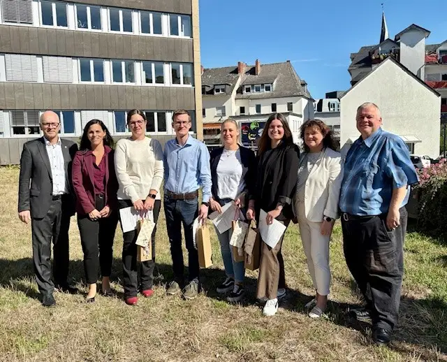 Acht Menschen stehen für ein Gruppenfoto im Freien vor einem Gebäude.